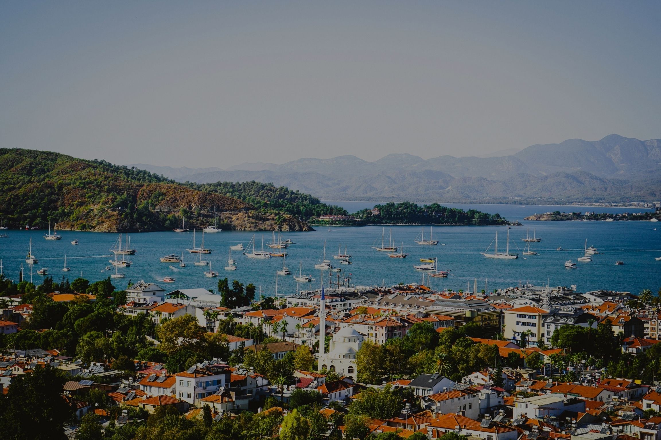 Scenic view of Fethiye city with marina, yachts, peninsula, and turquoise coastline – a top destination for luxury airport transfers in Turkey.